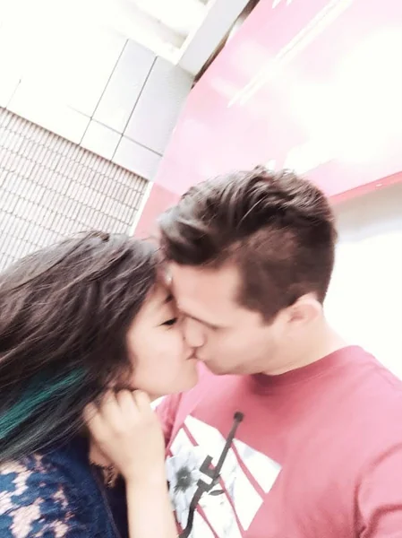 Un beso juntos frente a una pared rosa